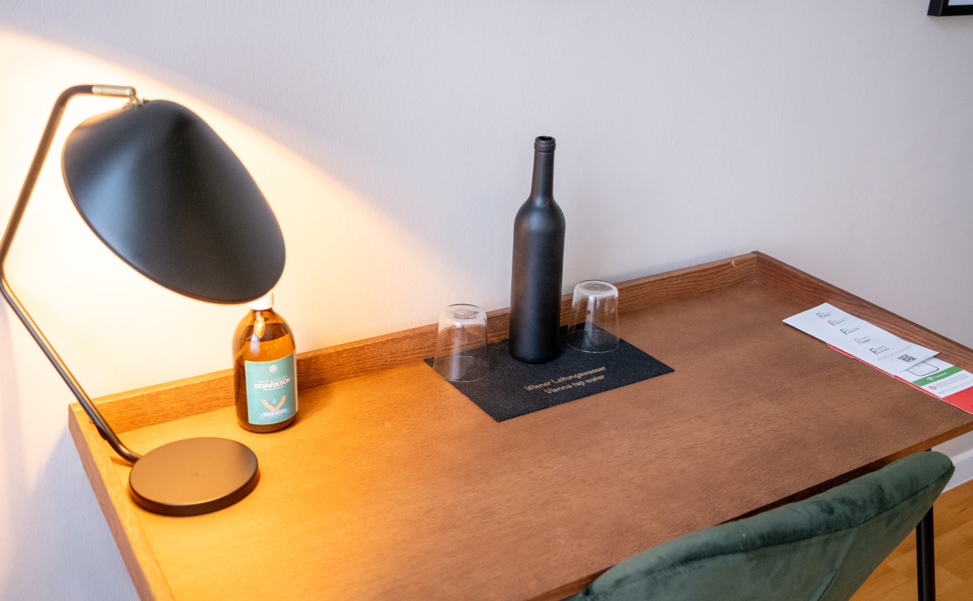 A desk with a lamp, bottle, two glasses, and a pamphlet
