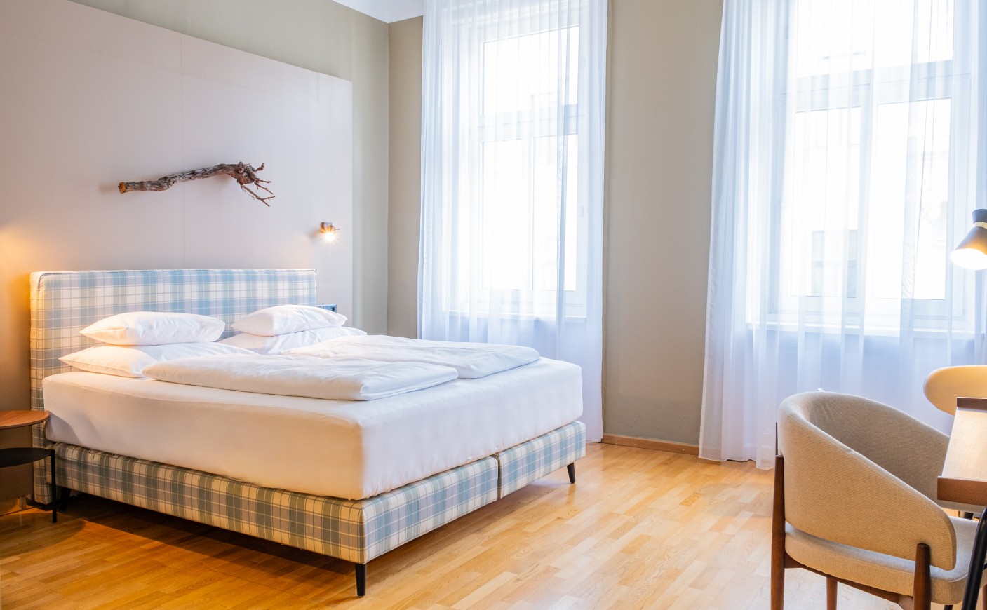 A bright bedroom with a plaid double bed and large windows