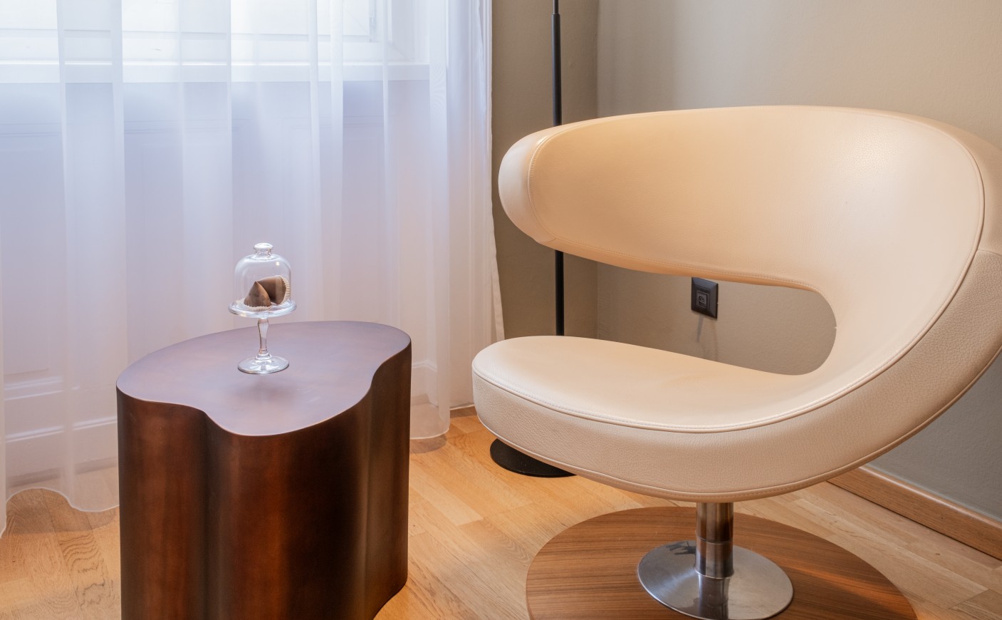 Modern beige chair beside a wooden table with a decorative item under glass